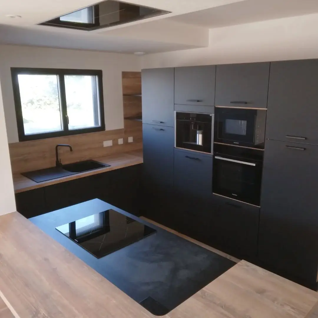Cuisine avec îlot central, façades noir mat et plan de travail bois — installée par Agencement Lennon à Landivisiau.